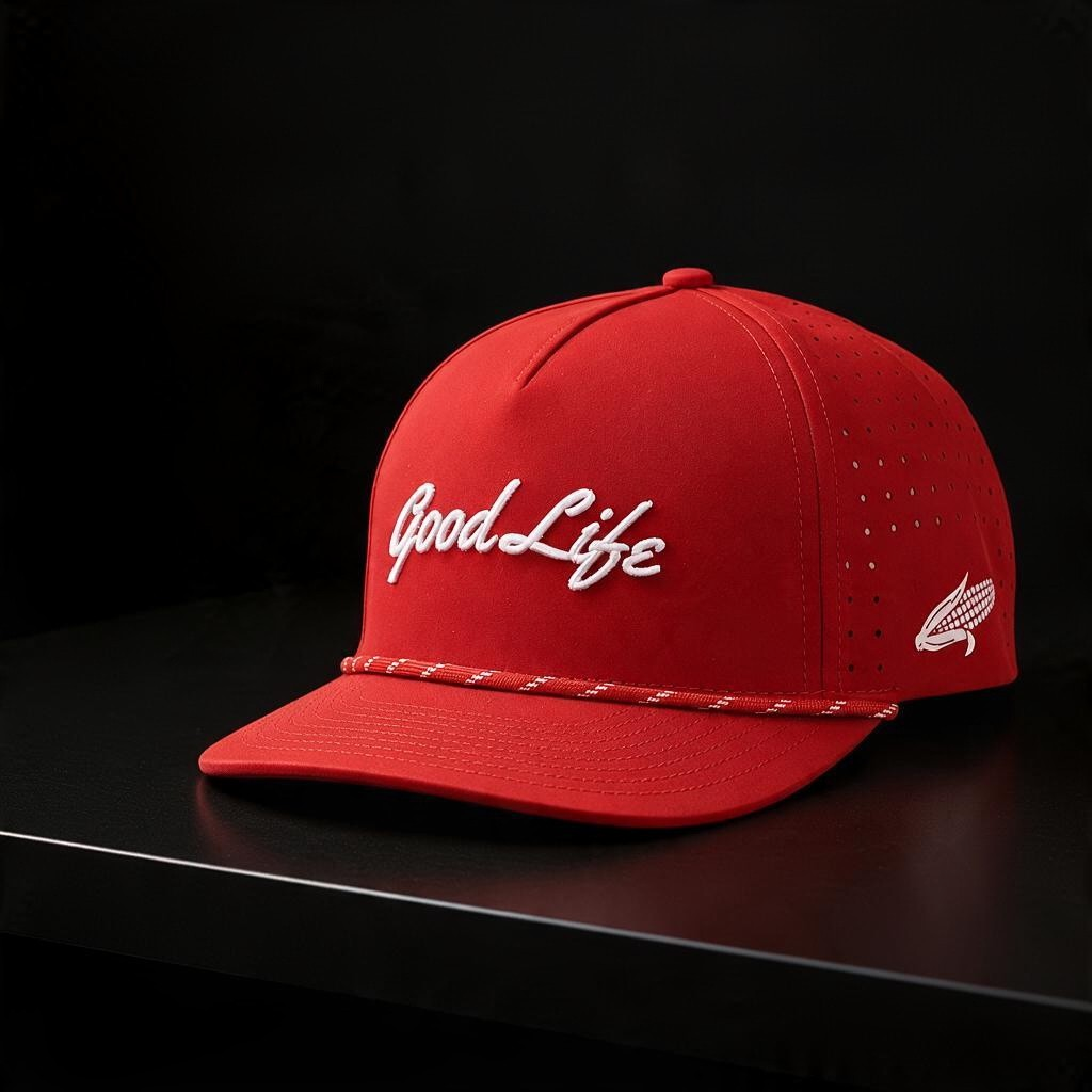 A red structured snapback hat with white embroidered 'Good Life' script on the front, a thin red-and-white rope detail across the visor, and a small white side logo, photographed on a dark surface against a black background.