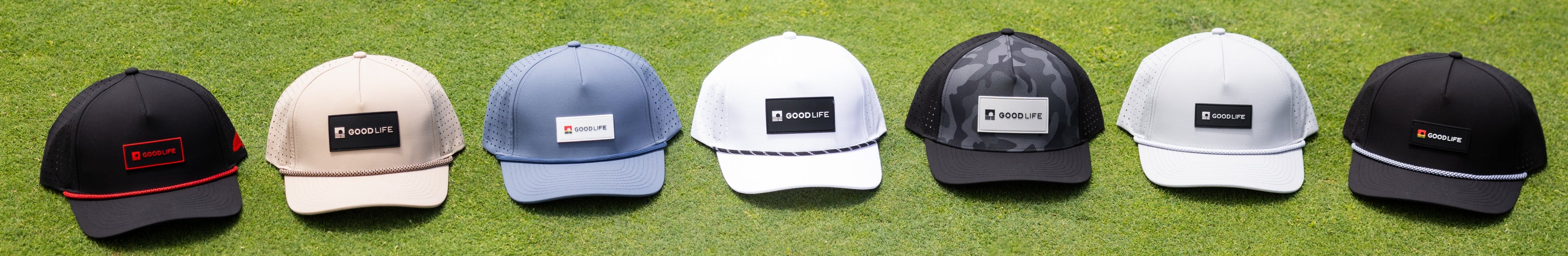 Seven golf hats in various colors arranged on a grassy field