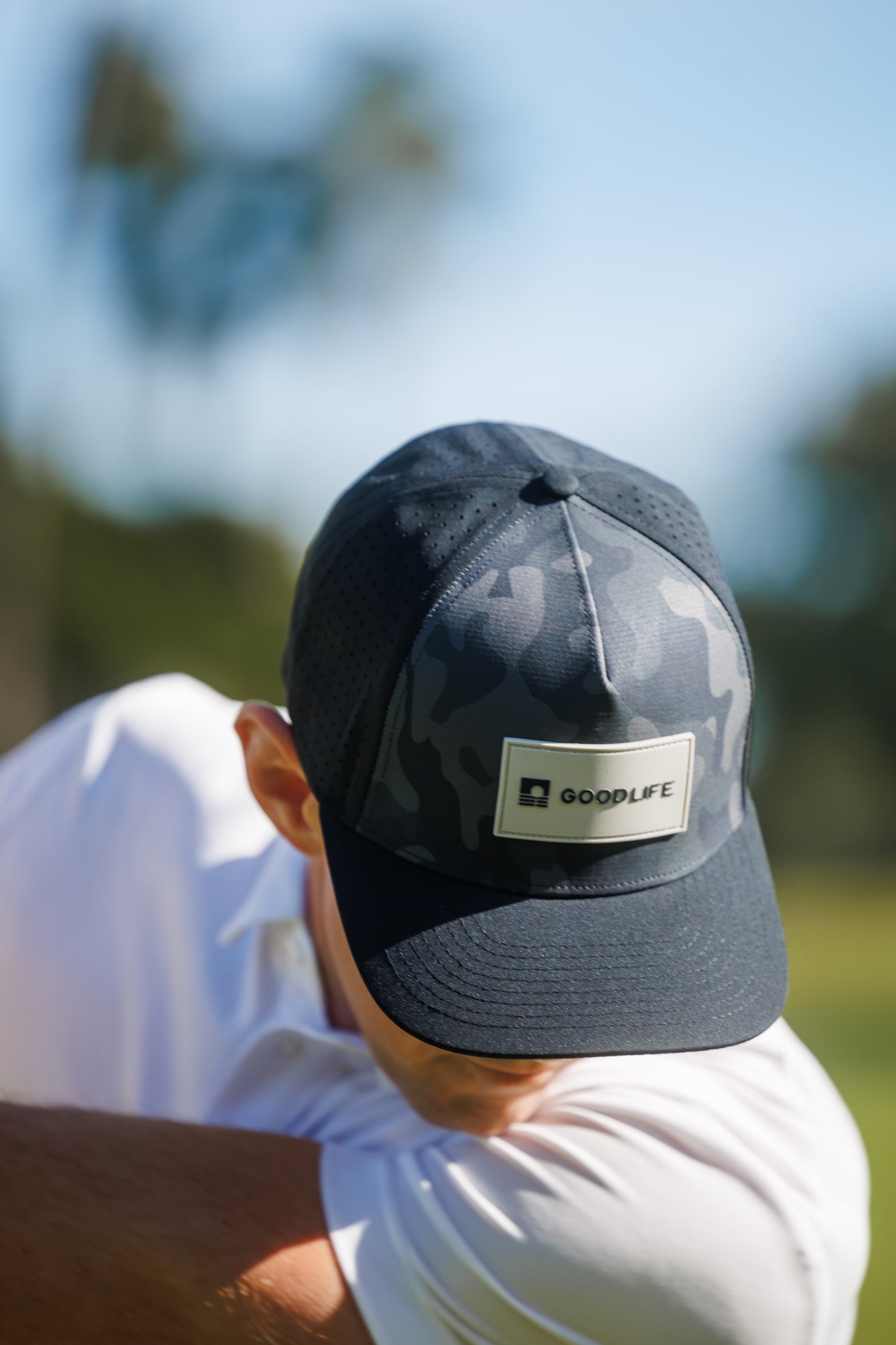 Person wearing a black cap with a GoodLife logo outdoors