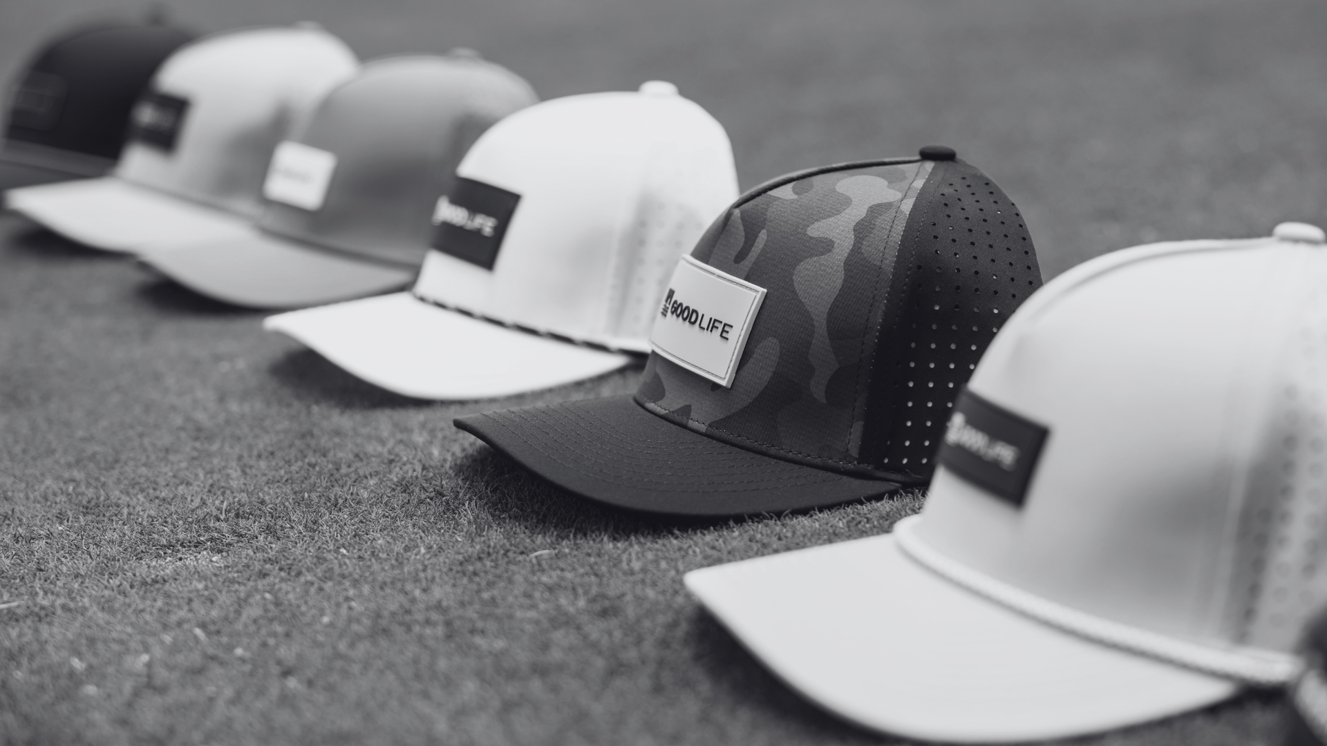 A row of snapback trucker hats lined up on a textured gray surface, shown in black and white. The hats feature a white front panel and visor, dark mesh back panels, and a central patch label with the brand name 'WOOLIFE'.