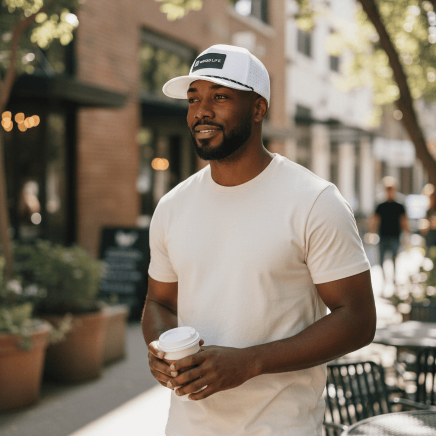 Man holding a coffee cup on a city street wearing a Good Life Golf Performance Classic White Snapback with black and white PVC patch water and sweat resistant perforated sides.  