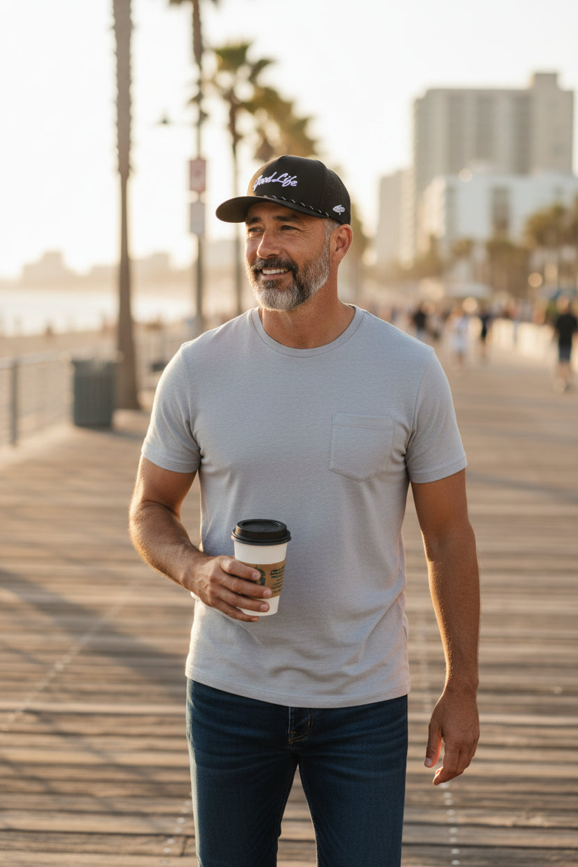 Man holding a coffee cup on a boardwalk with palm trees and buildings in the background